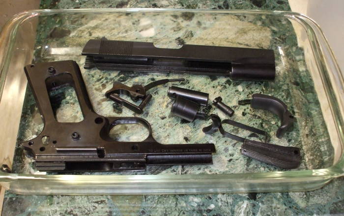 Bluing removal, removing bluing from gun parts with a vinegar bath. The parts are in a glass dish and covered with vinegar.