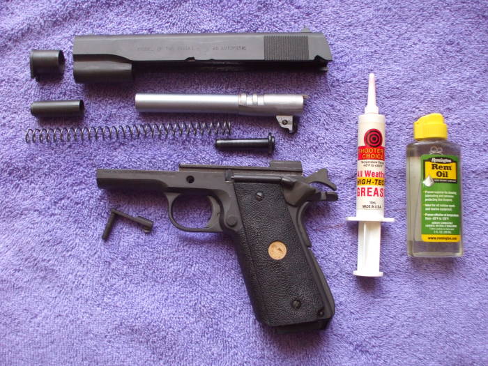 Parkerized M1911 pistol parts ready for lubrication and reassembly. Red 'all weather high-tech' grease and a small bottle of 'Rem Oil' containing teflon.